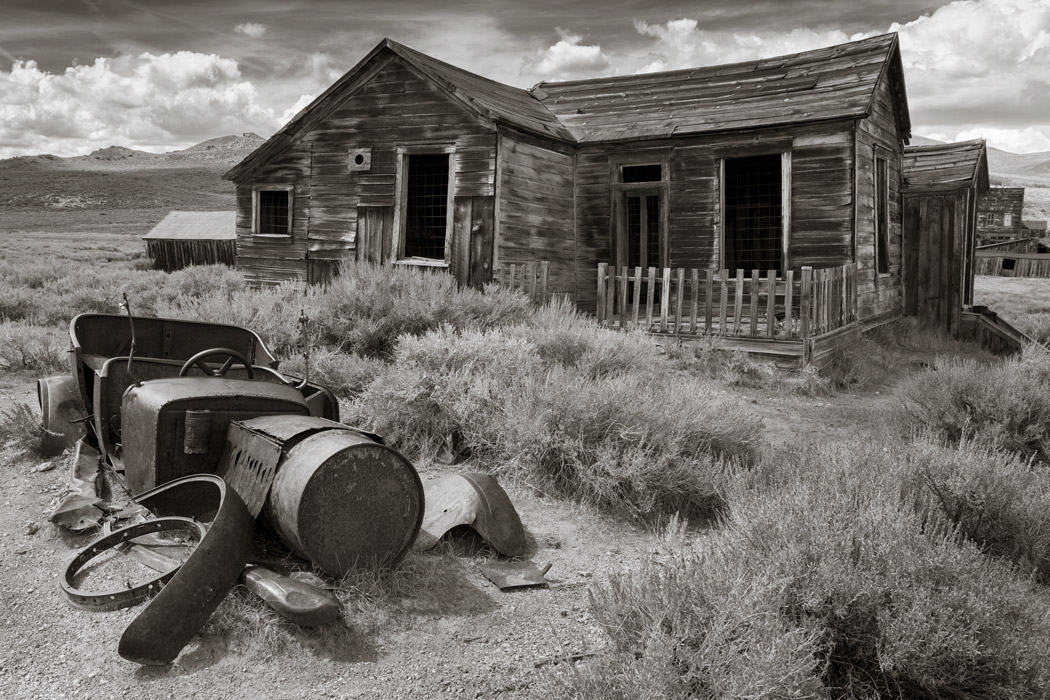 Rusted car frame in front of a Bodie abandoned house